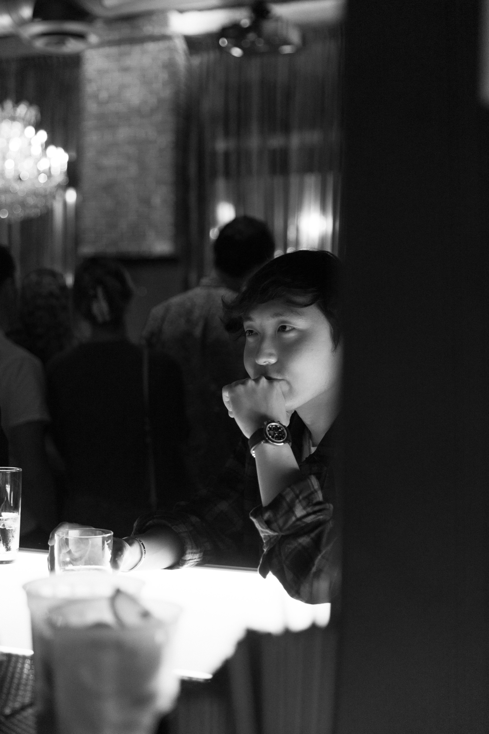 Black-and-white portrait of Mir Hwang at a bar, hand resting against his chin